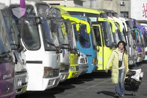 一位回家的旅客經過?？吭谄囌纠镎b待發的大客車前
